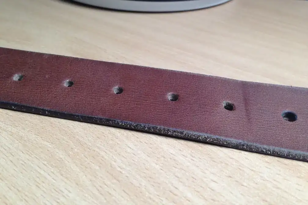 Tramo de un cinturón de cuero marrón con sus agujeros, apoyado sobre una mesa de madera clara